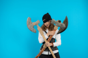 Young pirate girl holding axes and stand on blue background
