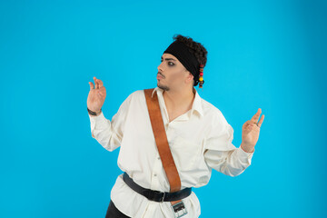 Young handsome pirate stand on blue background and don't know what to do