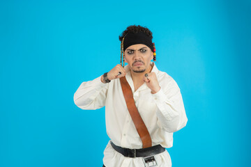 Angry Young pirate squeeze his feet and looking at camera. Young man standing blue background.