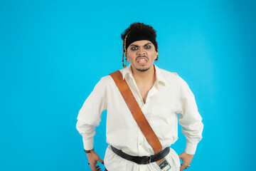 Portrait of a young angry pirate stand on blue background.
