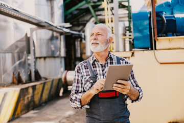 A senior factory supervisor walks around the facility with a tablet in his hands and monitors the works.