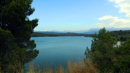 Large reservoir lake in the mountains, very blue water, pine trees on the shore, an island in the distance, mountains in the distance, beautiful landscape, Beniarres, Spain