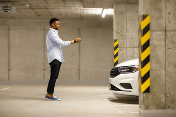 African american man with car keys in front of car in underground parking.