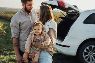 Young Caucasian Family Enjoying Road Trip, Mother and Father with Little Daughter Outdoors with SUV Car on the Background