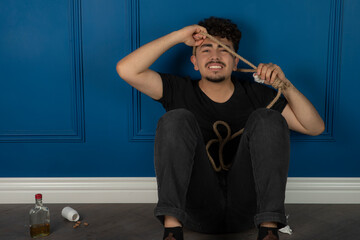 Young man sitting on the ground and putting a rope to his neck