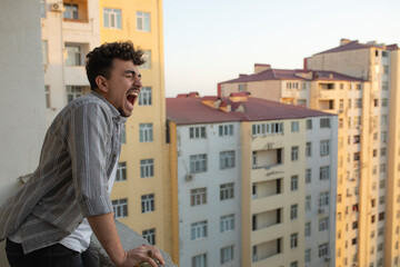 Exhausted young man screaming from balcony.