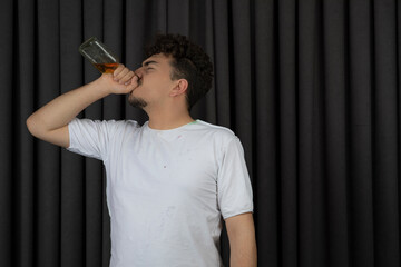 Young man drinking alcohol on the black background.