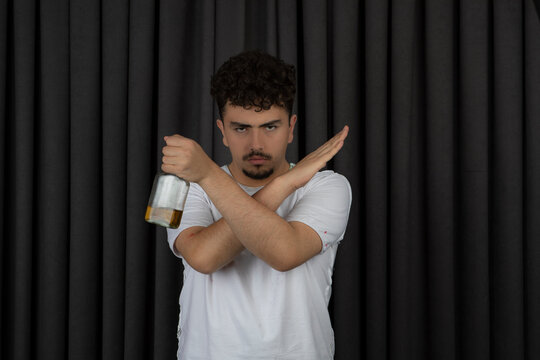 Young man holding bottle of alcohol and cross his hands.