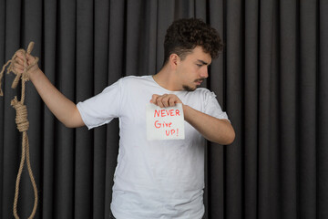 Depressed young guy holding motivating text and suicide rope