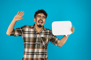 Creative young guy holding white idea board and dancing on blue background