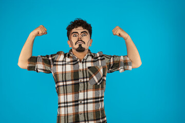 Young man stands on blue background and squeezed his biceps