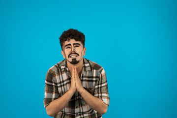 A man man with pop-art makeup stands on blue background and praying