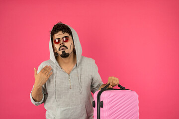 Portrait of a young guy with creative makeup holding pink suitcase and stand on red background