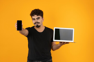 Portrait of a young man with pop art makeup holding computer and point his phone to the camera
