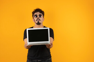 Creative young man with sunglasses holding a computer and stand on orange background.