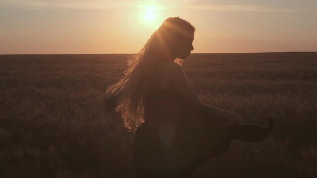 young woman in black dress dramatic choreography dance on the wheat field in a silhouette of the red sunset