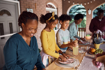 Fototapeta na wymiar African American multi-generation family setting dining table on patio.