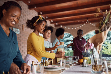 Happy black little girl and her extended family preparing dining table on patio.