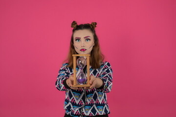 Portrait of young girl wearing colorful fantasy makeup and holding sand and clock