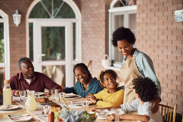 Happy black woman enjoys with her extended family during meal on patio.