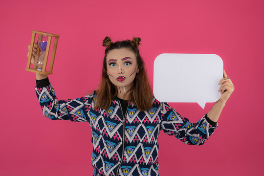 Young girl wearing fantasy makeup and stand on pink background. Beautiful girl holding idea board and sand clock.