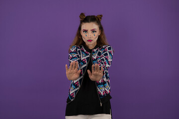 Young beautiful girl wearing fantasy makeup and gesturing stop on purple background