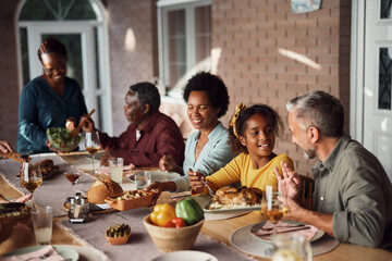 Happy multiethnic family enjoys while having meal at dining table on patio.