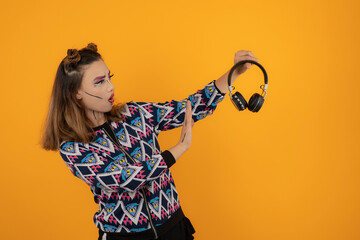 Portrait of young girl wearing creative makeup and holding headphones while gesturing NO