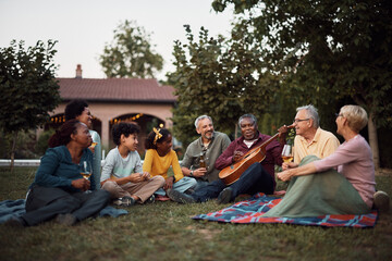 Happy multiracial extended family enjoys while senior black man is playing acoustic guitar in...