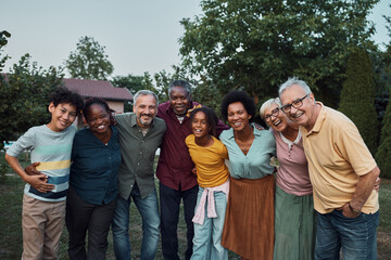 Portrait of embraced multi-ethnic extended family in backyard looking at camera.