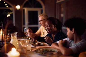 Black senior woman enjoys while eating dinner with her family on patio.