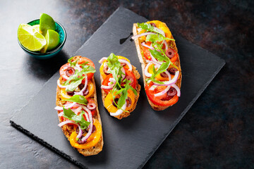 Spanish tapas on a dark background. Vegan tapas with tomatoes, onions, greens and olives. Healthy sandwiches on slate board. Top view. Copy space