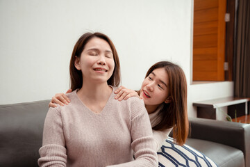 Asian young daughter massaging mid age mother for relax enjoy together happy family at home, relieve office syndrome concept.