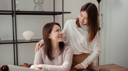 Asian lover family of mother and daughter using laptop computer together for shopping sitting on desk workplace hugging leisure love at home happiness insurance concept.