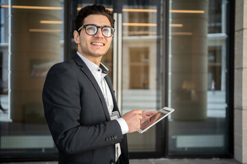 A businessman man with glasses works near the office uses a tablet