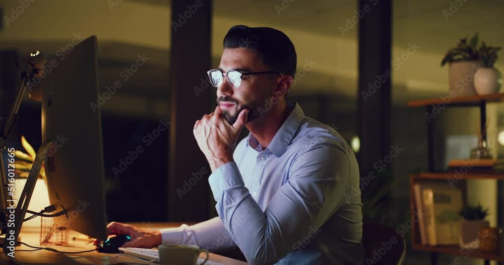 Poster Young business man looking thoughtful while reading an email on a desktop computer and working late at night. One serious corporate male designer doing overtime to meet a deadline in a dark office