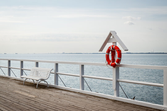 Lifebuoy at pier with empty bench in Gdynia Orlowo, Poland. Travel destination at coastline of Baltic sea