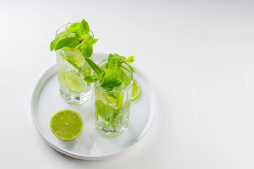 Mojito cocktail on a white background. Two glasses of mojito with mint and lime on a white plate. Summer drink concept. Copy space