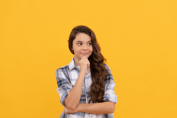 pondering teen child in checkered shirt with long curly hair on yellow background