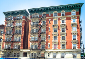Red brick residential building with black metal emergency stairs. Somewhere in Harlem, Manhattan,...