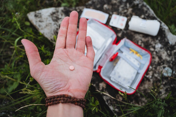 A pink tablet lies in the hand, first aid for poisoning in a hike, a first aid kit for emergency...