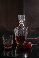 whiskey in a glass decanter on a piano with a glass of whiskey with a red rose next to it against the background of smoke from fog cigarettes