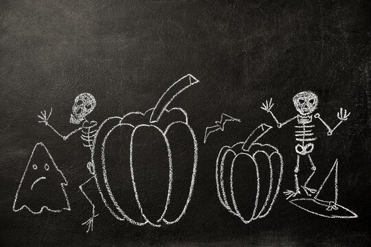 Skeletons, pumpkins and a ghost bat painted on a chalk board. Halloween drawing on chalkboard background.