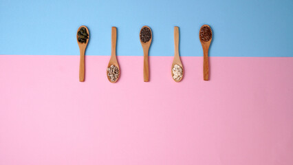 Healthy food flat lay. Wooden spoons lined up and filled with cereal seeds. Modern pink blue healthy food concept. Copy text.