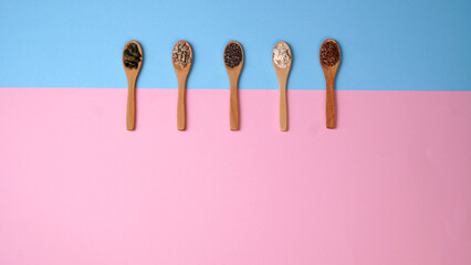Flat lay of arranged wooden spoons with various healthy seeds on a blue and pink background. Copy text. Healthy food concept.