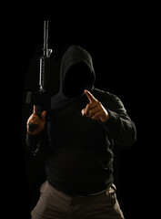 Portrait of a terrorist wearing a black hoodie holding a m16 rifle on a black background.concept of...