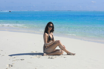 Fototapeta na wymiar girl model in a black bikini on the white sand by the ocean
