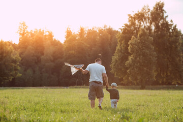 Family vacation. Summer outdoor photo of a father and son flying a kite in a meadow. A picture...