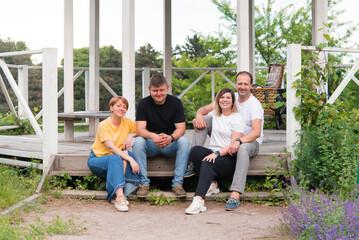 family of four sitting on the steps of a gazebo in the park and smiling at the camera