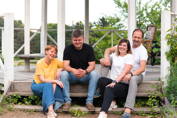 family of four sitting on the steps of a gazebo in the park and smiling at the camera